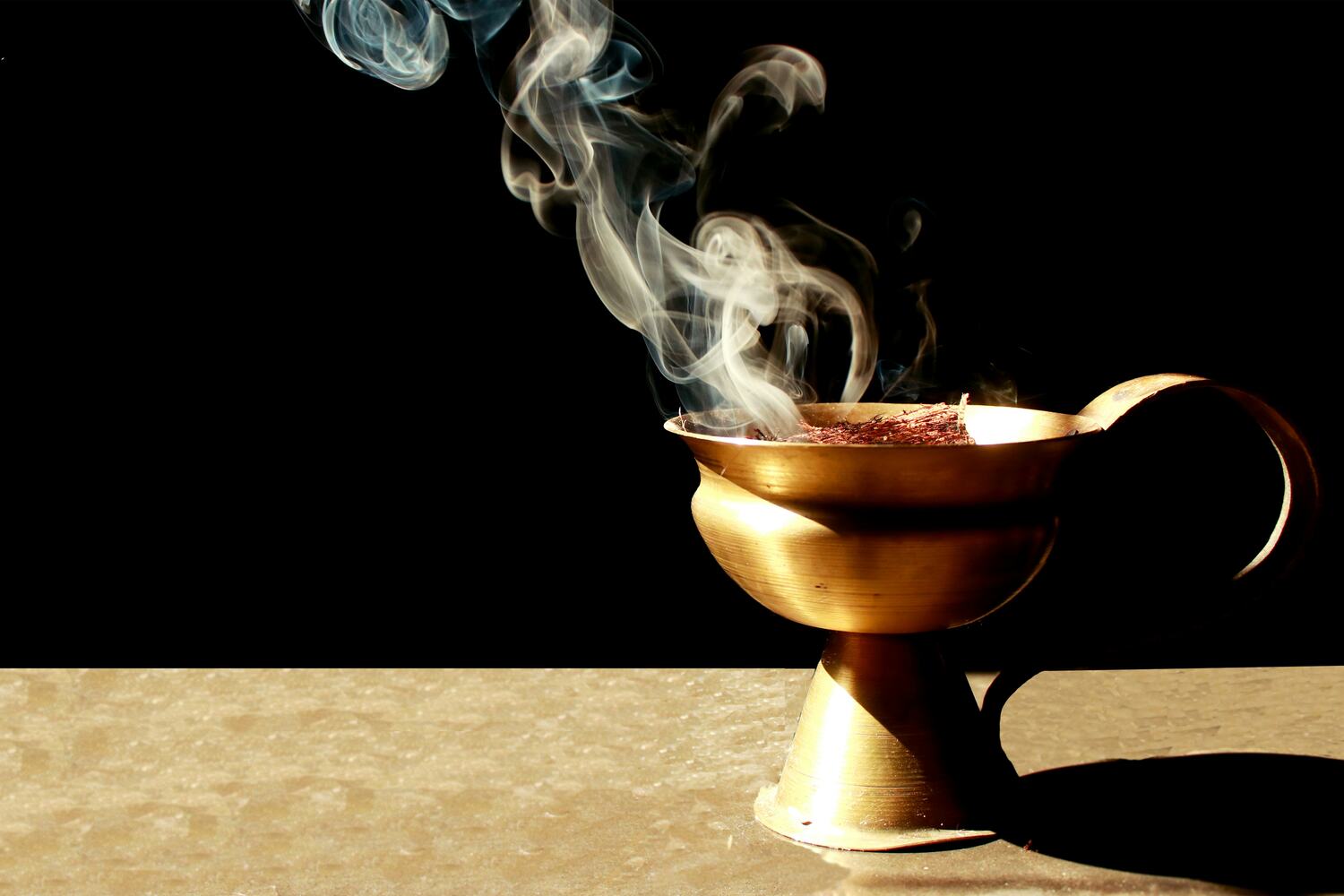Une image dramatique montrant de l'encens brûlant dans un brûleur en laiton traditionnel sur un fond sombre. La fumée s'élève doucement, créant une atmosphère mystique et séduisante, reflétant un ingrédient clé des parfums envoûtants de Heritage Parfum Paris.